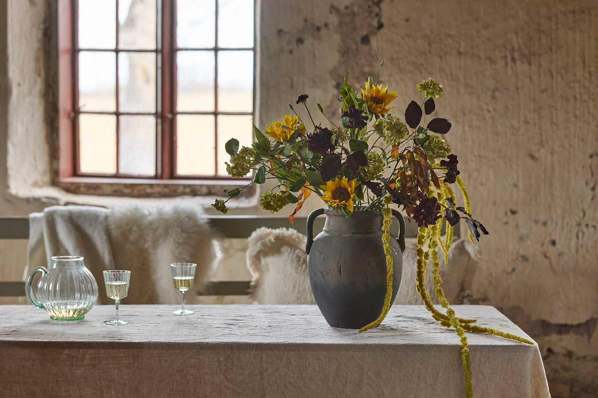 Bild på en vas som står på ett matbord mes massor av konstväxt kvistar/blommor- bild till konstväxt kategorin