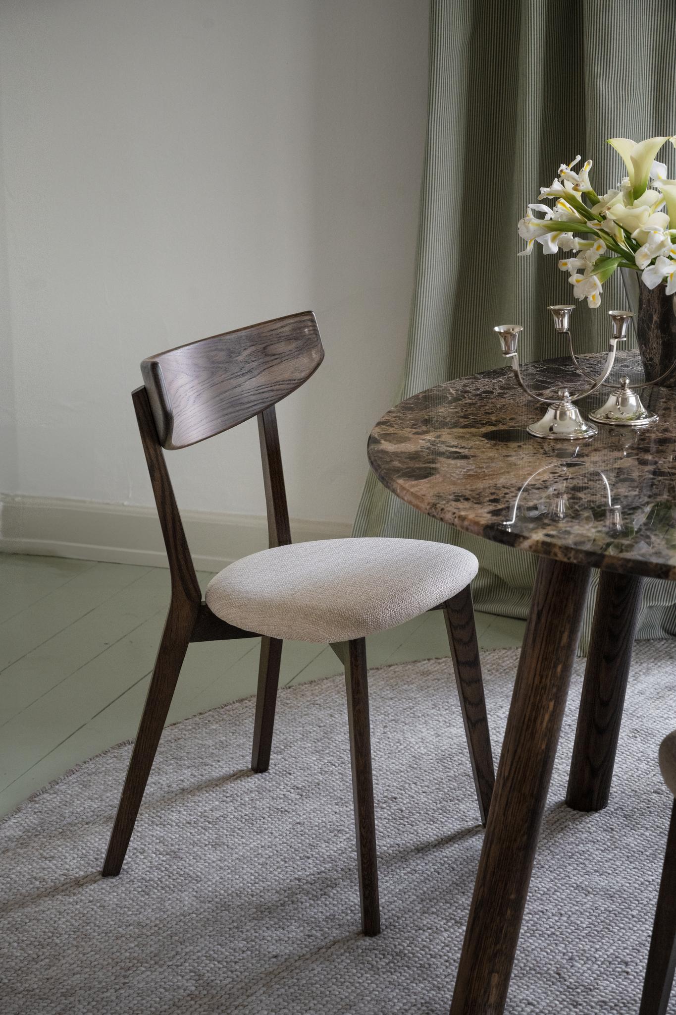 Matstol i mörkt trä med beige klädsel vid runt marmorbord med silverljusstakar och vita blommor