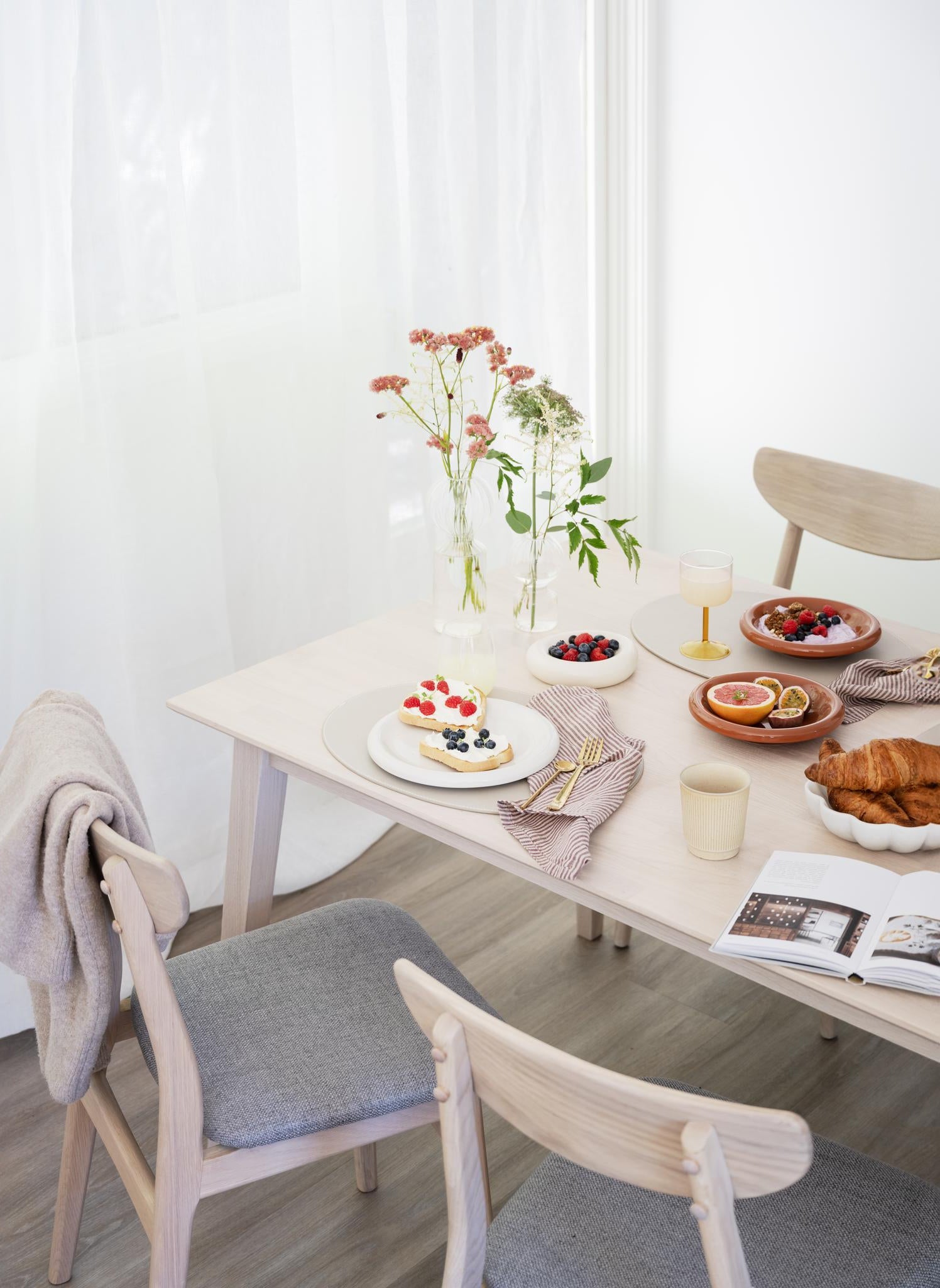 Ljust matbord i trä dukat med frukost, croissanter, bär och blommor i skandinavisk stil