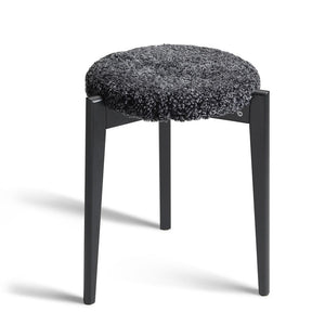 Rund pall med svart träram och grå fluffig sits i fårskinn