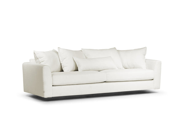 Vit modern soffa med lös dyna och mjuka kuddar på svart sockel mot vit bakgrund