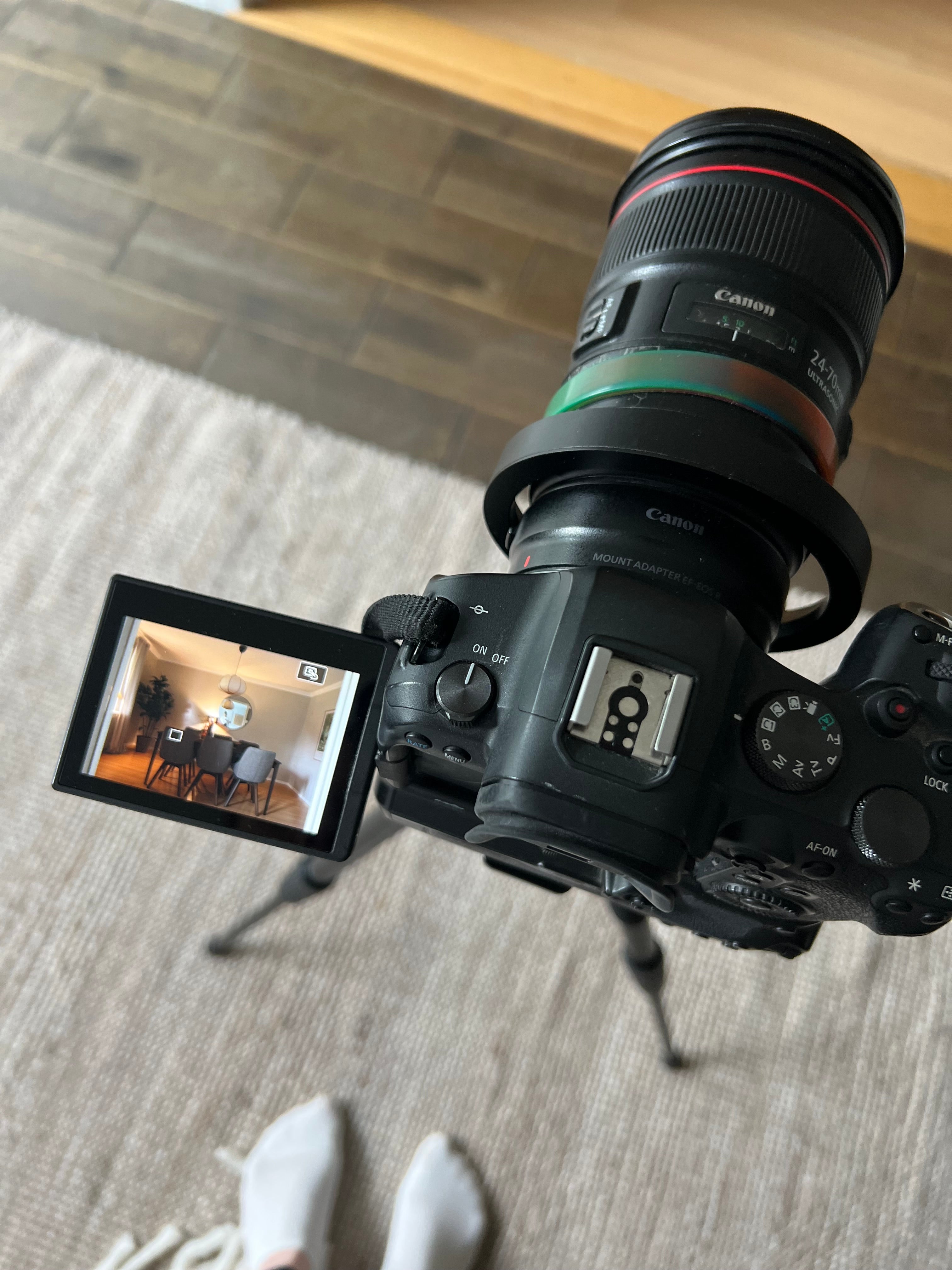 Canon kamera med teleobjektiv och mount adapter, uppfälld LCD-skärm visar interiör, placerad på vit textil