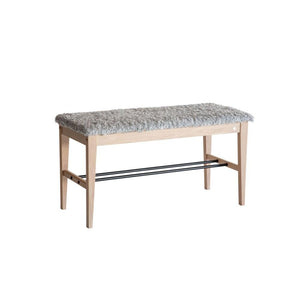 Hallbänk med grå fårskinnsdyna och ljust trästativ med hylla för skoförvaring