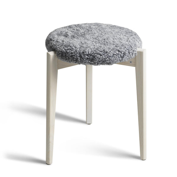 Pall med grå fårskinnsdyna och vitlaserade träben i skandinavisk design