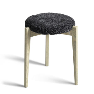 Pall med mörkgrå fårskinnsdyna och ben i ljust trä