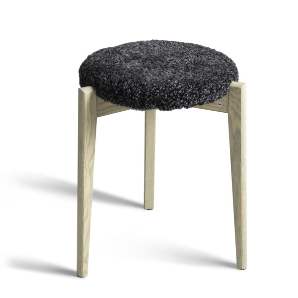 Pall med mörkgrå fårskinnsdyna och ben i ljust trä