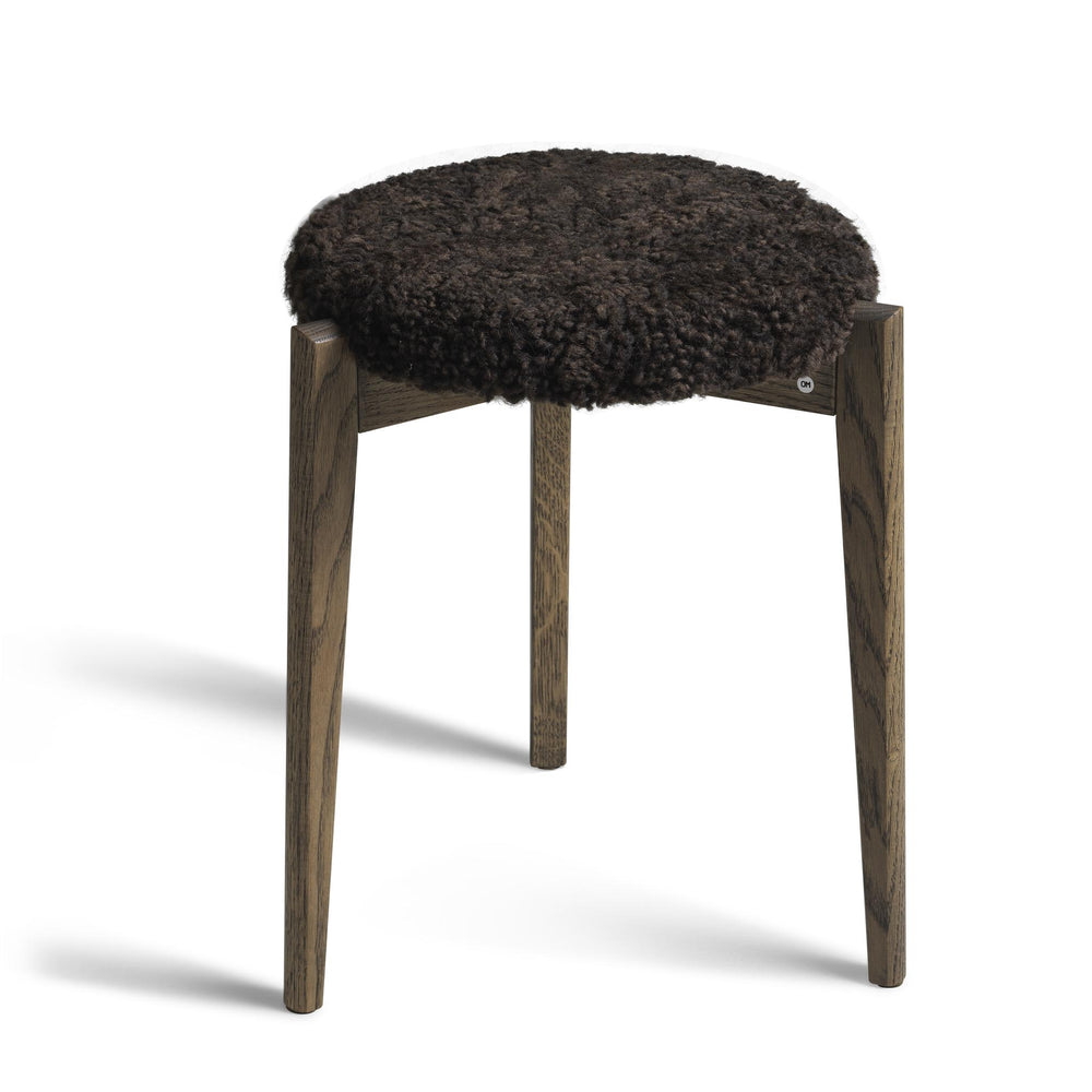 Pall med svart fårskinn på ekben, rund sits med tre träben i naturlig ekfärg