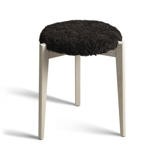 Pall med svart fårskinnsdyna och ljusa träben i ek mot vit bakgrund