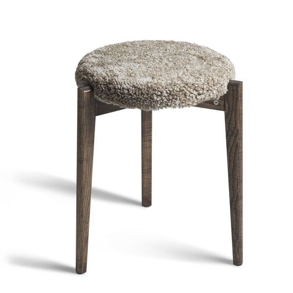 Rund pall med beige fårskinnsdyna och mörkbruna träben i skandinavisk design