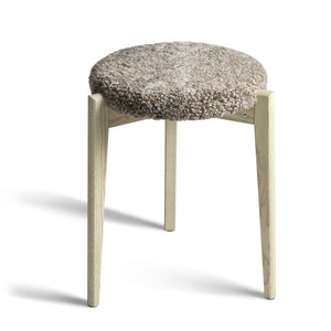 Pall med tre träben i ljust trä och rund sits med fluffig fårskinnsdyna i beige