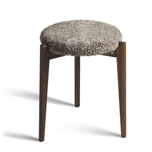 Pall med grå fårskinnsdyna och mörka träben i valnöt, skandinavisk design