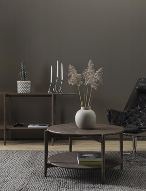 Stilrent vardagsrum med runt soffbord i mörkt trä, vit vas med torkade växter och minimalistisk inredning