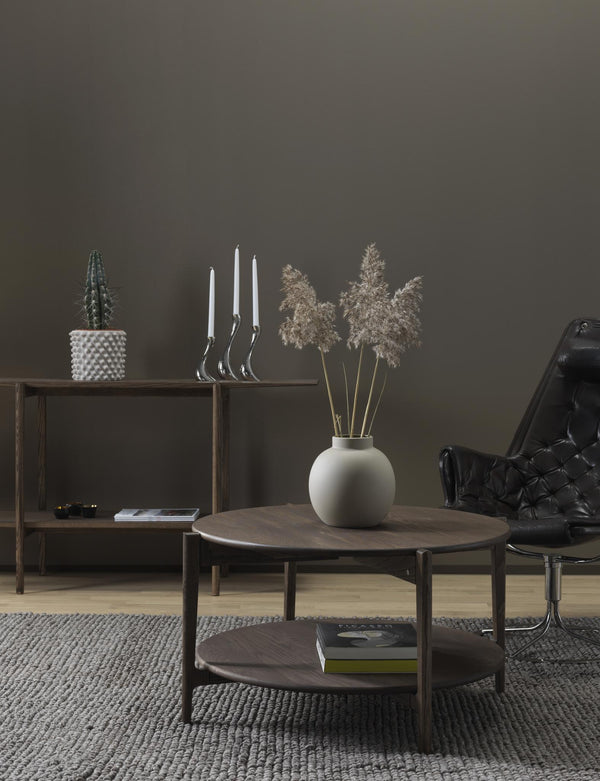 Stilrent vardagsrum med runt soffbord i mörkt trä, vit vas med torkade växter och minimalistisk inredning