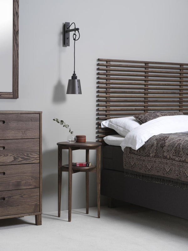 Sovrum i rustik stil med träsäng, sängbord, byrå och vägglampa i industriell design