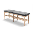 Hallbänk i ljust trä med grå fårskinnsdyna och två förvaring shyllor under sitsen