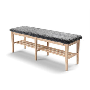 Hallbänk i ljust trä med grå fårskinnsdyna och två förvaring shyllor under sitsen