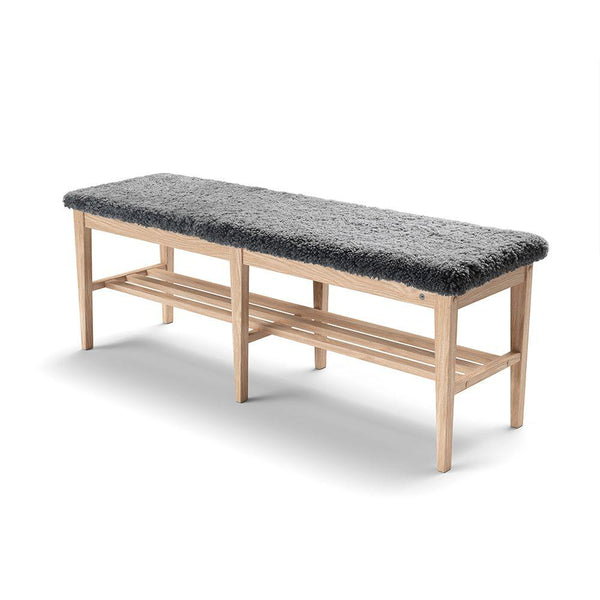 Hallbänk i ljust trä med grå fårskinnsdyna och två förvaring shyllor under sitsen