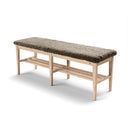 Hallbänk i ljust trä med grön sittdyna i fårskinn och två förvaringshyllor under sitsen