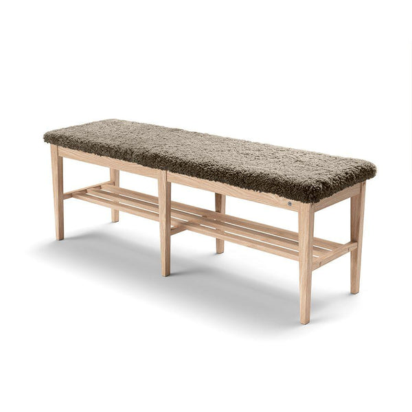 Hallbänk i ljust trä med grön sittdyna i fårskinn och två förvaringshyllor under sitsen