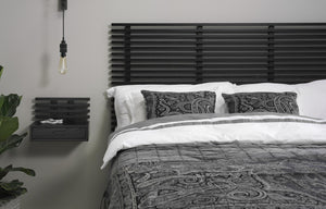 Modernt sovrum med svart ribbad sänggavel, vit sängkläder och grå paisleymönstrade kuddar och överkast