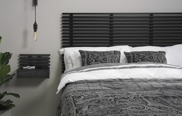 Modernt sovrum med svart ribbad sänggavel, vit sängkläder och grå paisleymönstrade kuddar och överkast