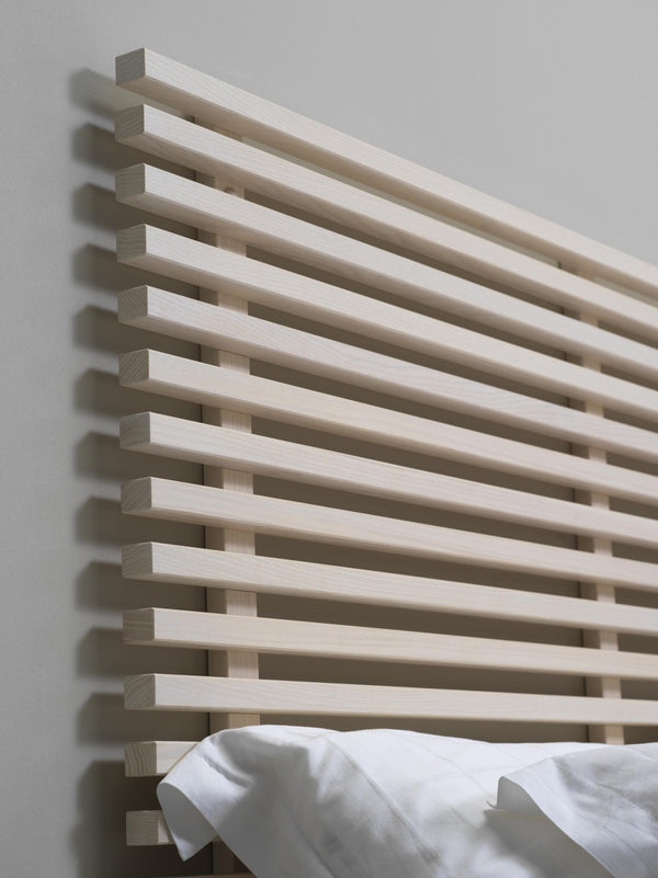 Ljust trä handdukstork med horisontella ribbor monterad på vit vägg med vit handduk