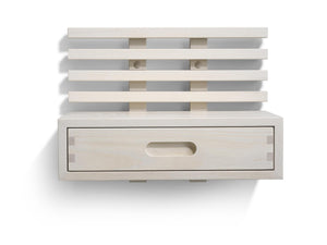 Väggmonterad sänghylla i ljust trä med ribbor och en utdragbar låda med oval handtagsöppning