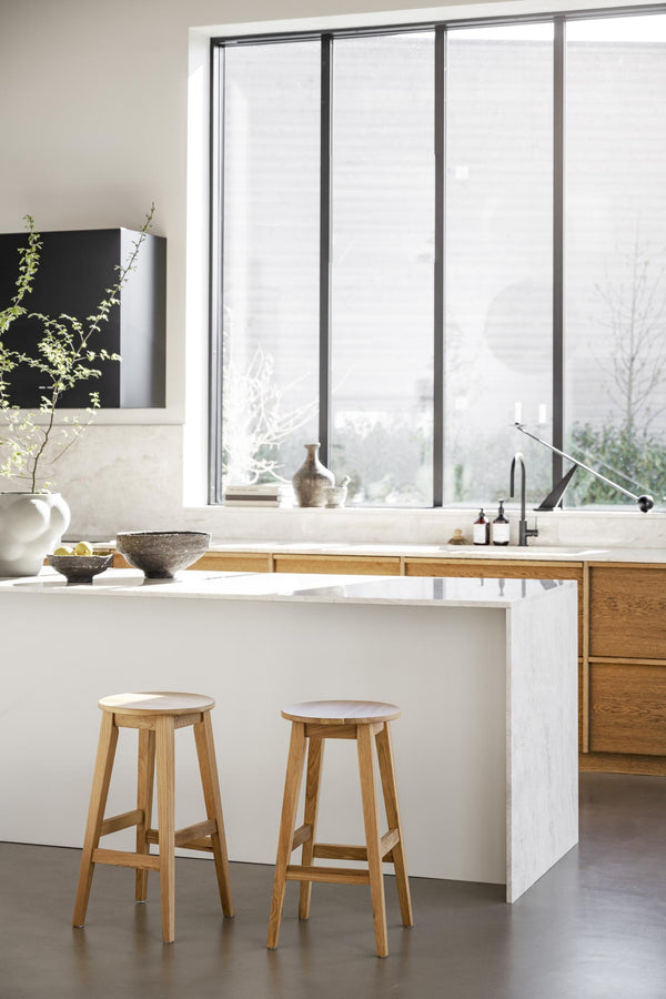 Modernt kök med vit marmorbänkskiva, träpallar och stora fönster med utsikt