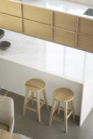 Två träpallar i ljust trä vid vit köksö med marmorbänkskiva och eklådor i modern skandinavisk stil