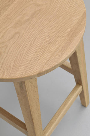 Rund träpall i ljus ek med synlig trästruktur och triangulära ben med fotpinnar