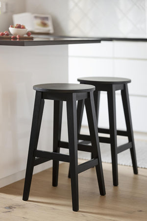 Två svarta träpallar vid vitt köksbord i modern skandinavisk inredning
