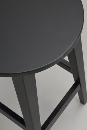 Närbild på rundad sits och ben på mörkgrå pall eller barstol med träkonstruktion