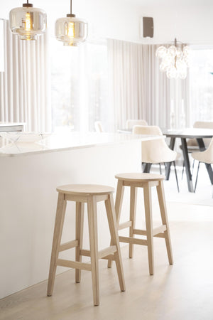 Ljust kök med träpallar vid köksö, vita stolar vid matbord och glas-pendellampor