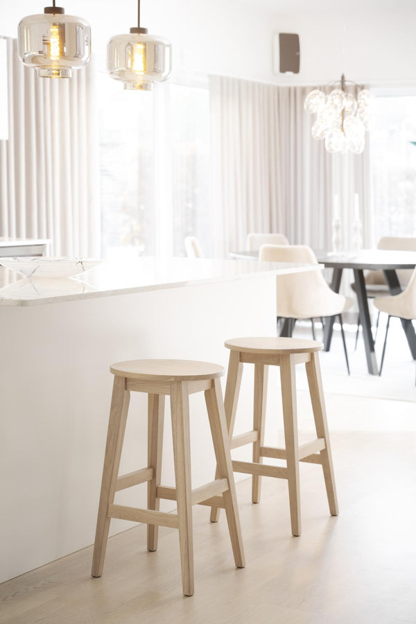 Ljust kök med träpallar vid köksö, vita stolar vid matbord och glas-pendellampor