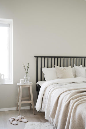 Minimalistiskt sovrum med svart spjälsäng, vita sängkläder och ljust trästol som sängbord