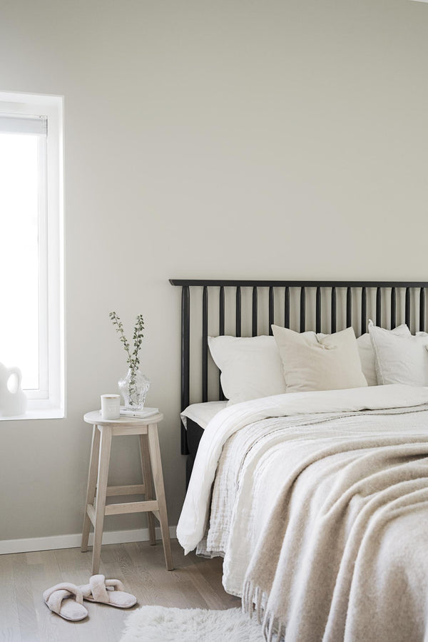 Minimalistiskt sovrum med svart spjälsäng, vita sängkläder och ljust trästol som sängbord