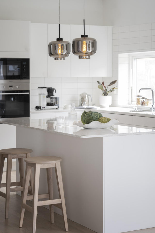 Modernt kök med vit köksö, ljusa träpallar och två gråa takpendlar i glas