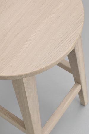 Närbilder på rund träpall i ljust trä med naturlig struktur och tre ben med förstärkande stag
