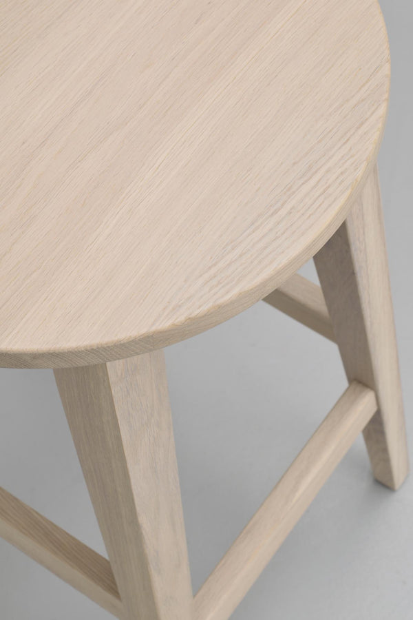 Närbilder på rund träpall i ljust trä med naturlig struktur och tre ben med förstärkande stag