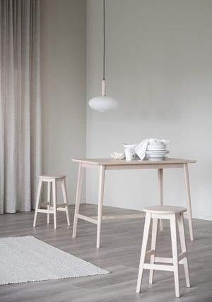 Ljus matgrupp i björk med ovalt bord och två pallar, vit taklampa och vita tallrikar i minimalistisk skandinavisk stil