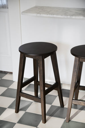 Mörk träpall med rund sits och fyra ben vid vit köksbänk med marmorskiva