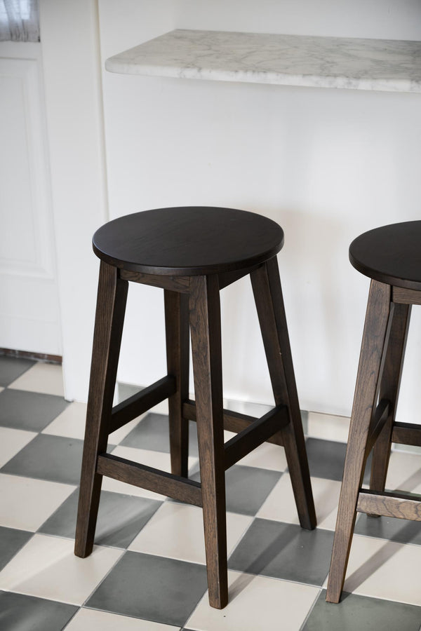 Mörk träpall med rund sits och fyra ben vid vit köksbänk med marmorskiva