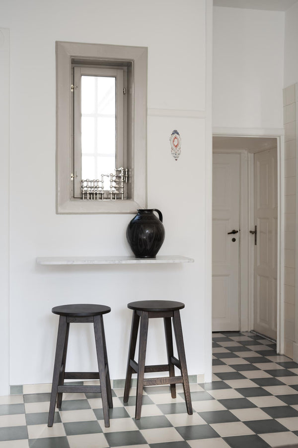 Två svarta träpallar under vit hyllplan med svart vas i minimalistiskt kök med rutigt golv