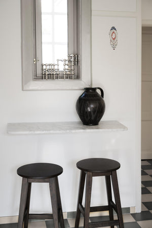 Två mörkbruna träpallar framför vit bardisk med svart vas och fönster med dekorativt galler