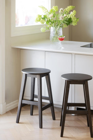 Två mörkbruna barstolar i trä framför vit köksbänk med blommor och drinkglas