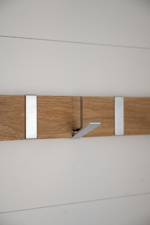 Krokbräda i ek med silverfärgade metallkrokar och beslag monterad på vit vägg