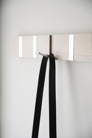 Klädhängare i ljust trä med vita krokar monterad på vit vägg, med svart bälte upphängt