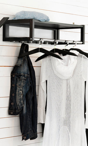 Svart hyllkroklist med klädhängare i metall monterad på vit vägg med jeansjacka och vit tröja