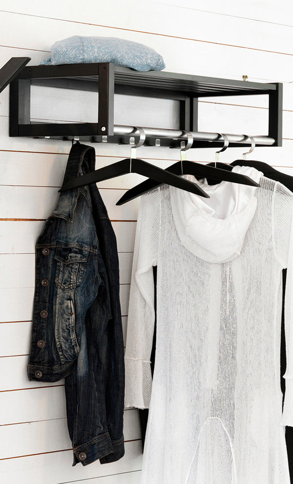 Svart hyllkroklist med klädhängare i metall monterad på vit vägg med jeansjacka och vit tröja