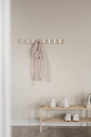 Ljus trähängare med vita krokar monterad på vägg, beige scarf hängande, träskoställ med vita sneakers nedanför